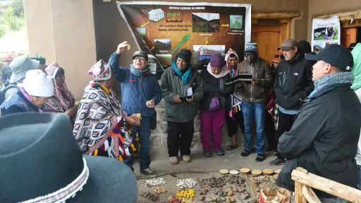 A group of people gather with crops on the floor in front of them and posters behind.
