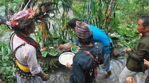 People holding trays of crops perform a ceremony next to a river.