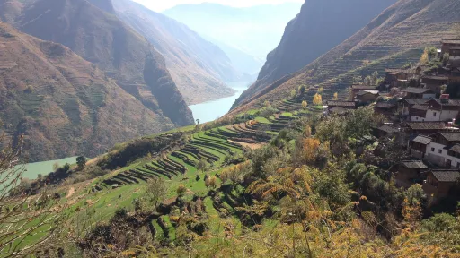 A scenic view of dwellings built in layers on the side of a mountain, with a lake and mountains in the background.