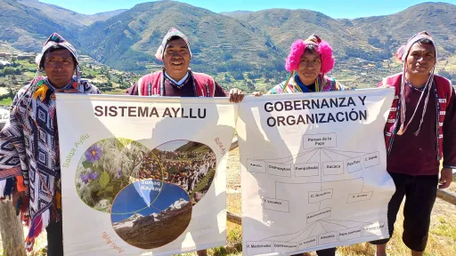 Four people hold up posters showing photos and flowcharts in front of a scenic mountain backdrop.