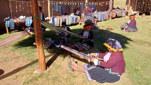 Women sit on the floor as they weave bright coloured products.
